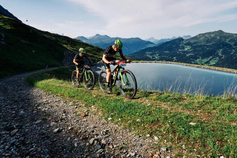 Two bikers peddling across a lake side path