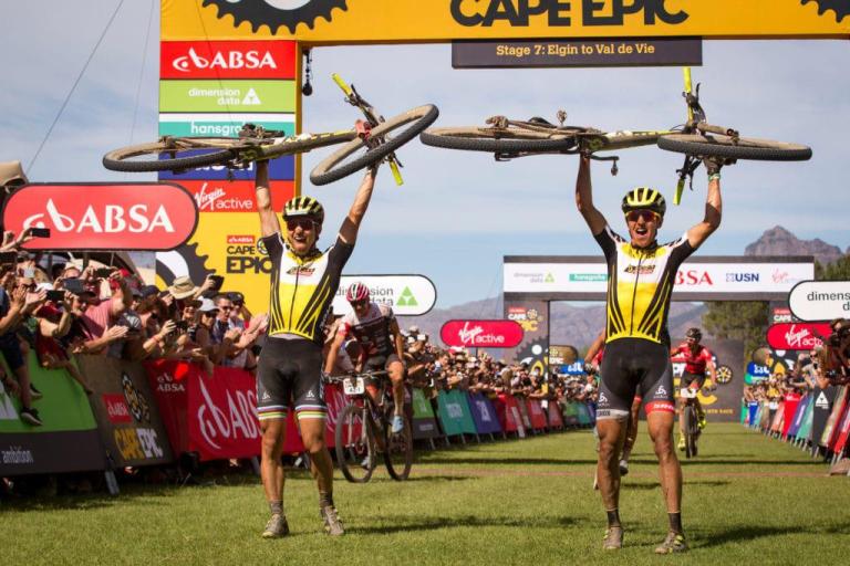 Two bikers after the finish line holding their bikes above their head