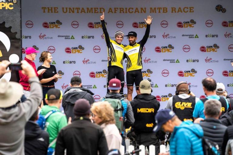 Two men posing under the Untamed African MTB Race poster