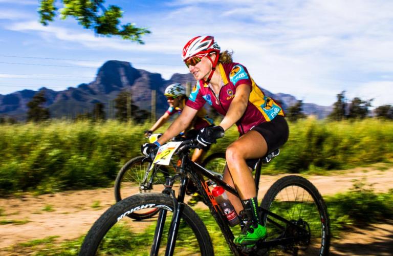 Two bikers racing past with a mountain in the background