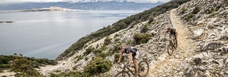 Two bikers on a mountain path with a lake in the background